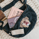 Black waist bag with bulldog design on a textured surface with books and phone.