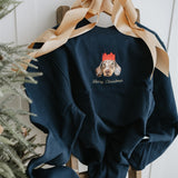 Navy blue sweatshirt with Christmas design on a wooden stool next to a decorated Christmas tree.