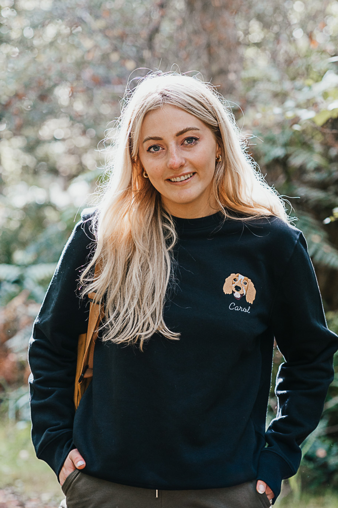 Woman smiling while wearing a custom embroidered sweatshirt with a hand-drawn pet portrait on organic cotton fabric
