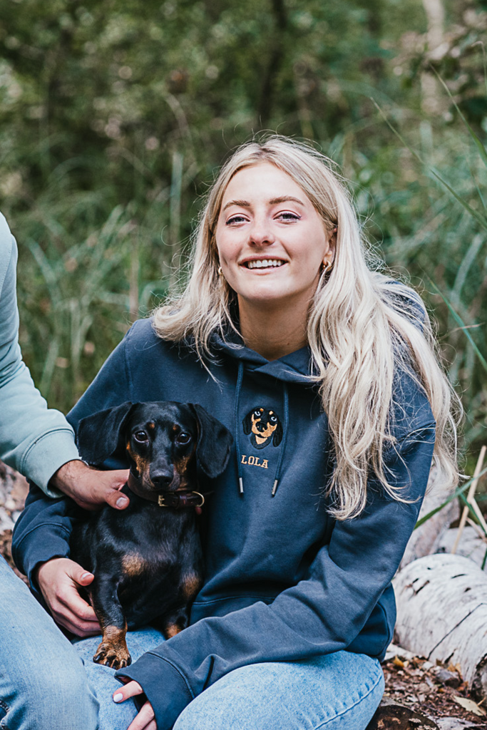 Woman smiling while wearing a custom embroidered hoodie featuring a hand-drawn pet portrait, the perfect personalised pet gift.